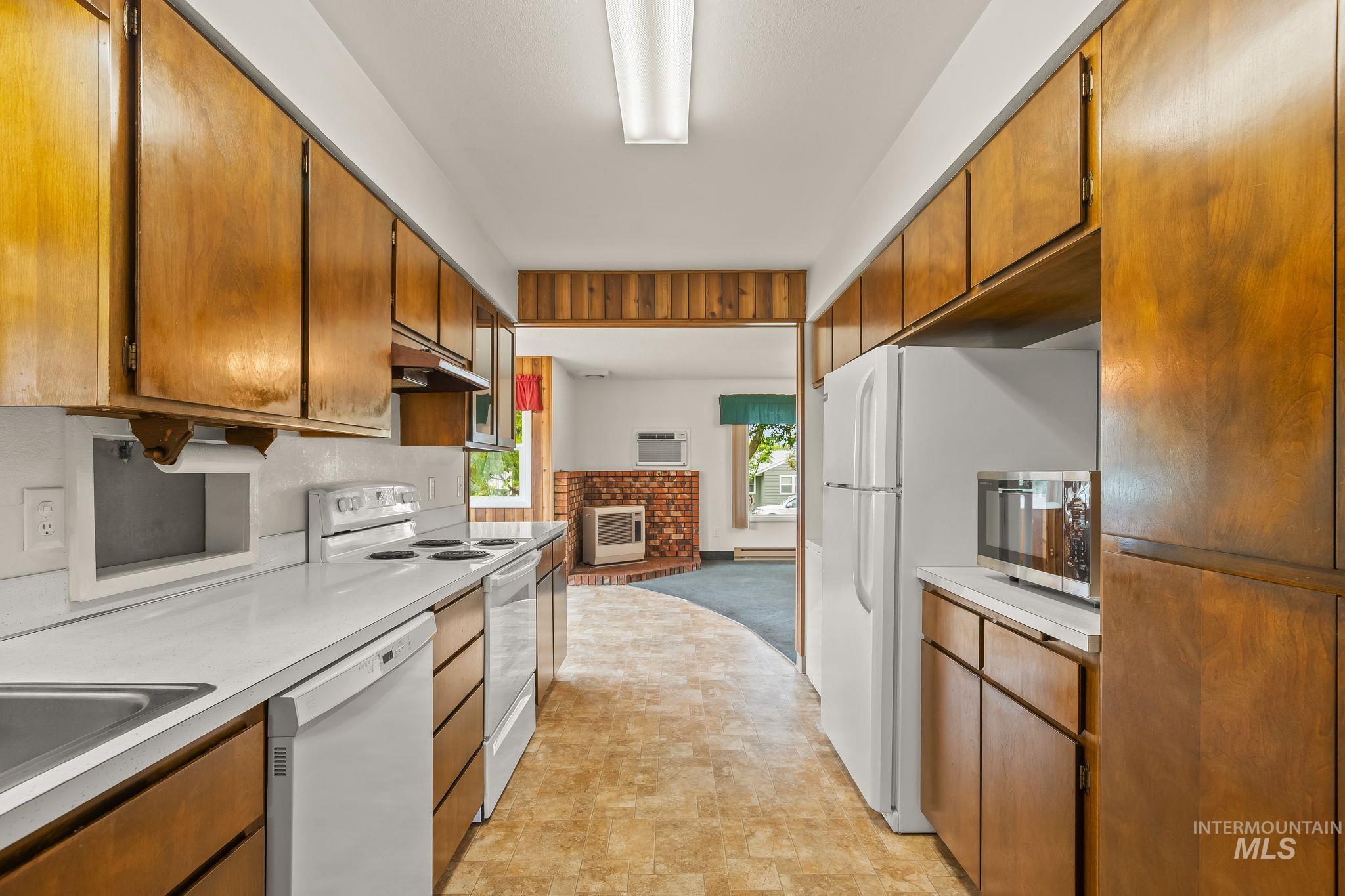 Galley kitchen featuring wood-finish cabinetry, white countertops, and integrated white appliances