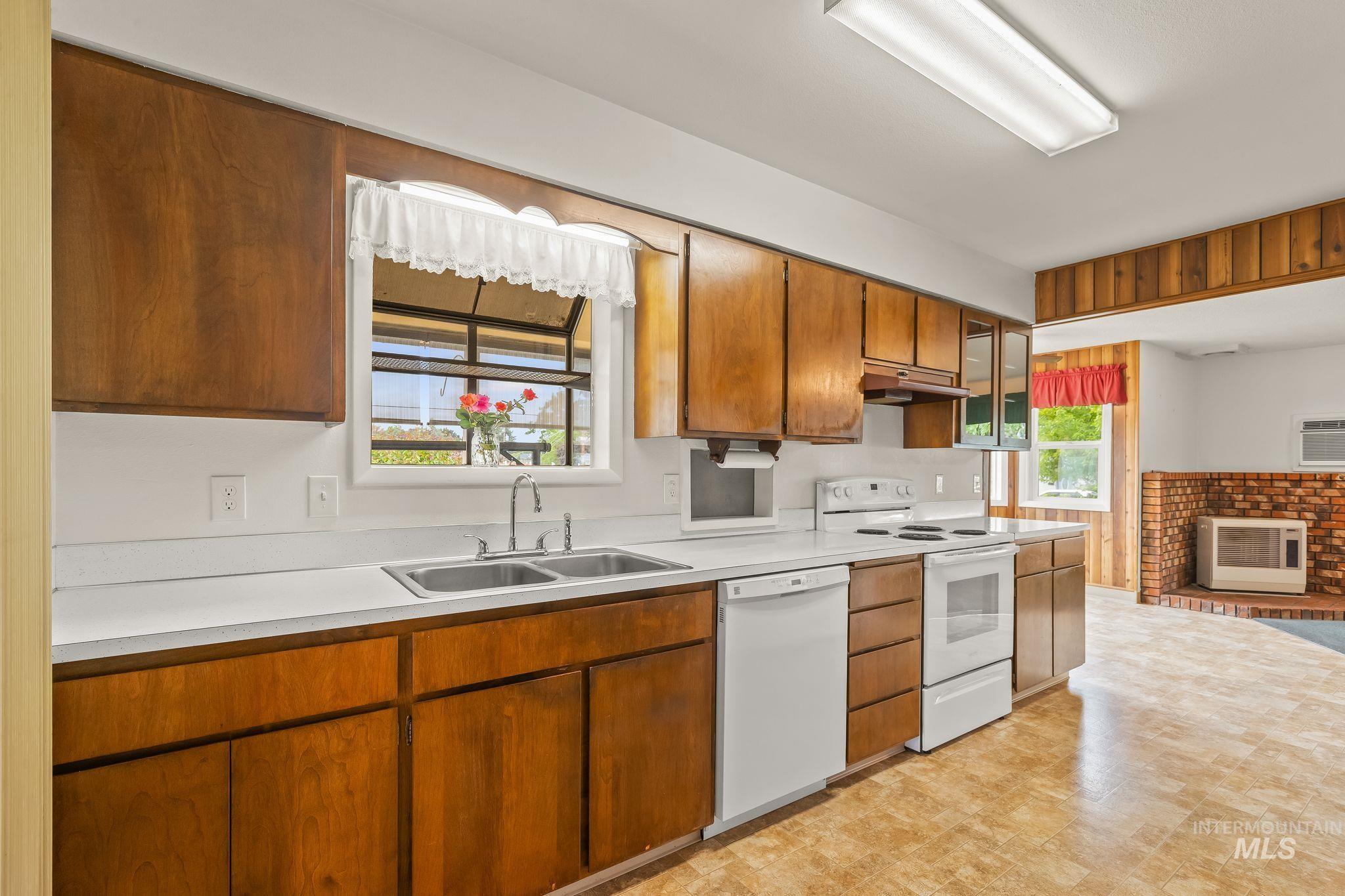 Kitchen featuring wood cabinetry, a double basin stainless steel sink, white countertops, and white appliances