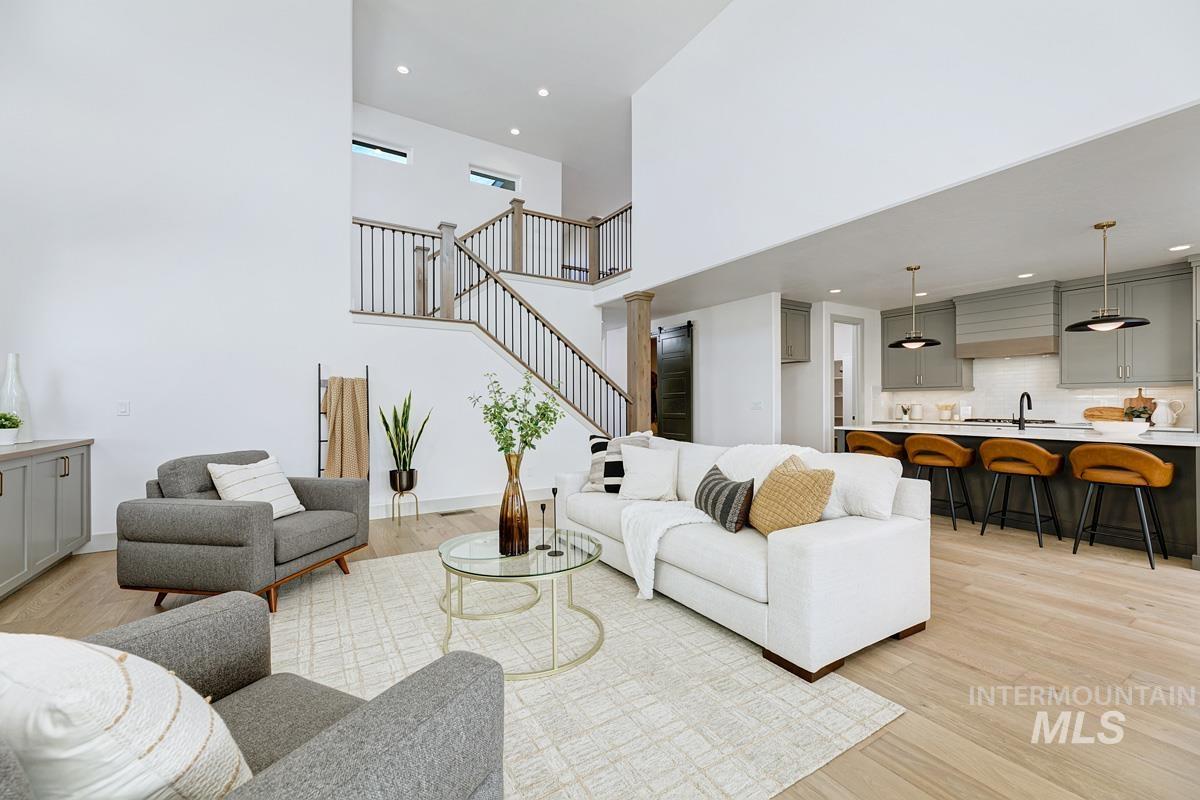 Living room with light wood-style floors, a towering ceiling, stairs, and recessed lighting