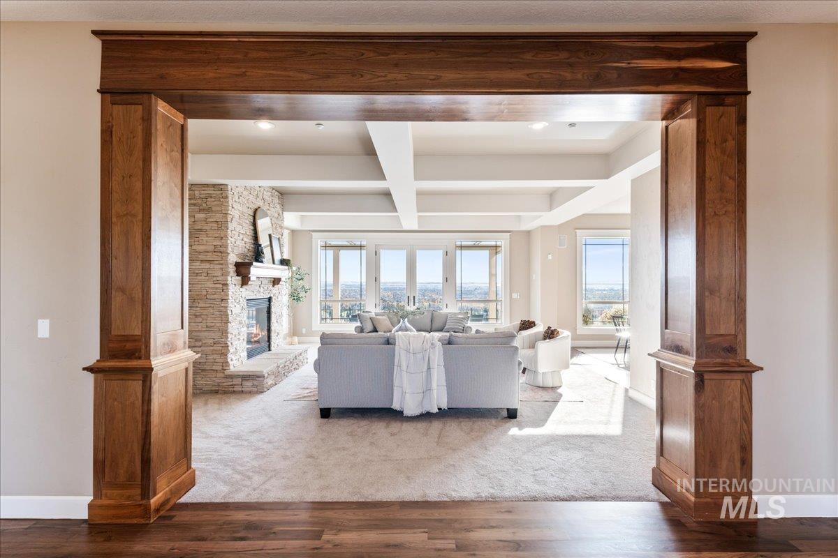 Living area with beamed ceiling, wood finished floors, coffered ceiling, a fireplace, and decorative columns
