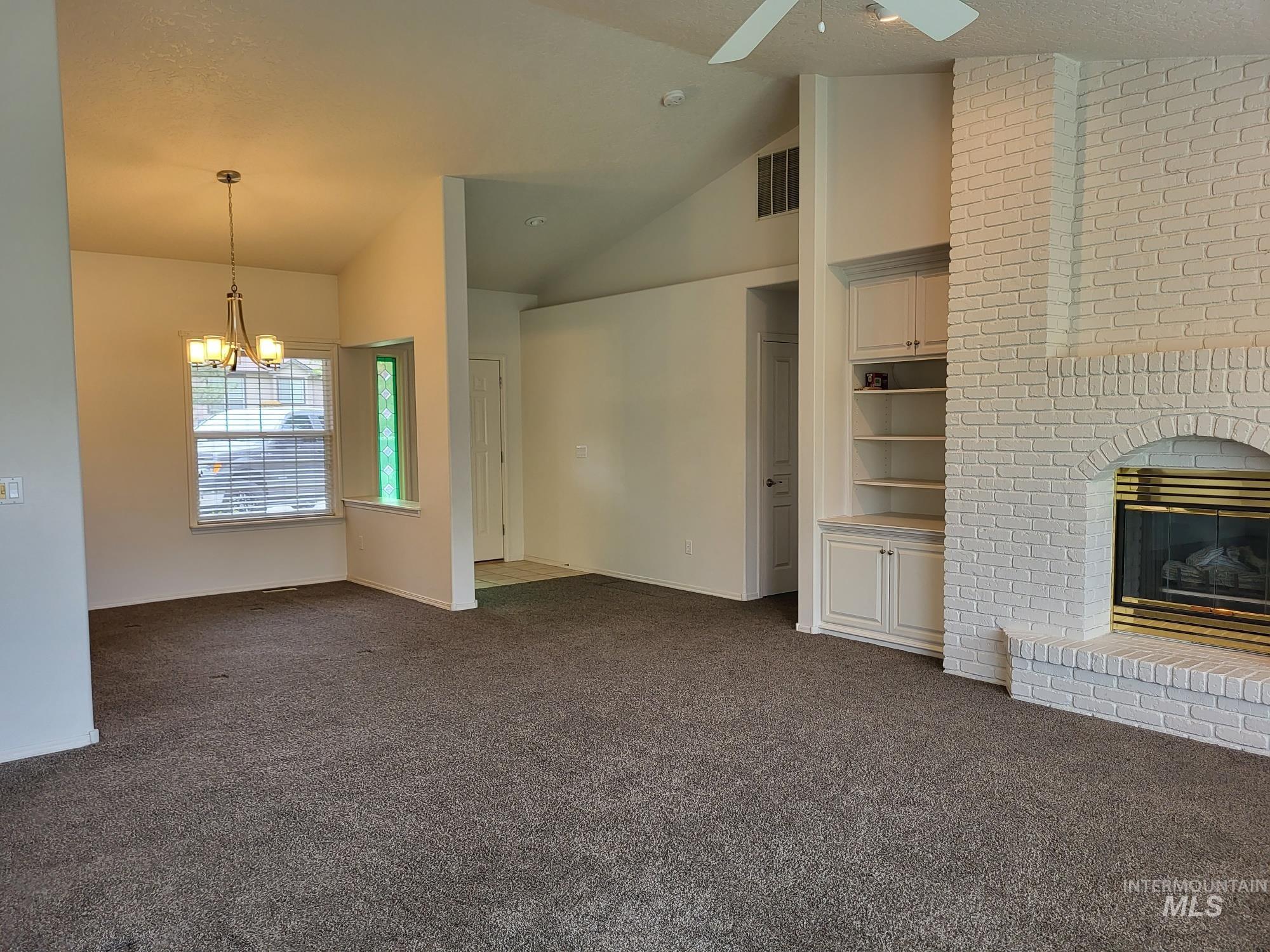 Living area featuring a painted brick fireplace, built-in cabinetry with shelving, vaulted ceilings, and ceiling fan