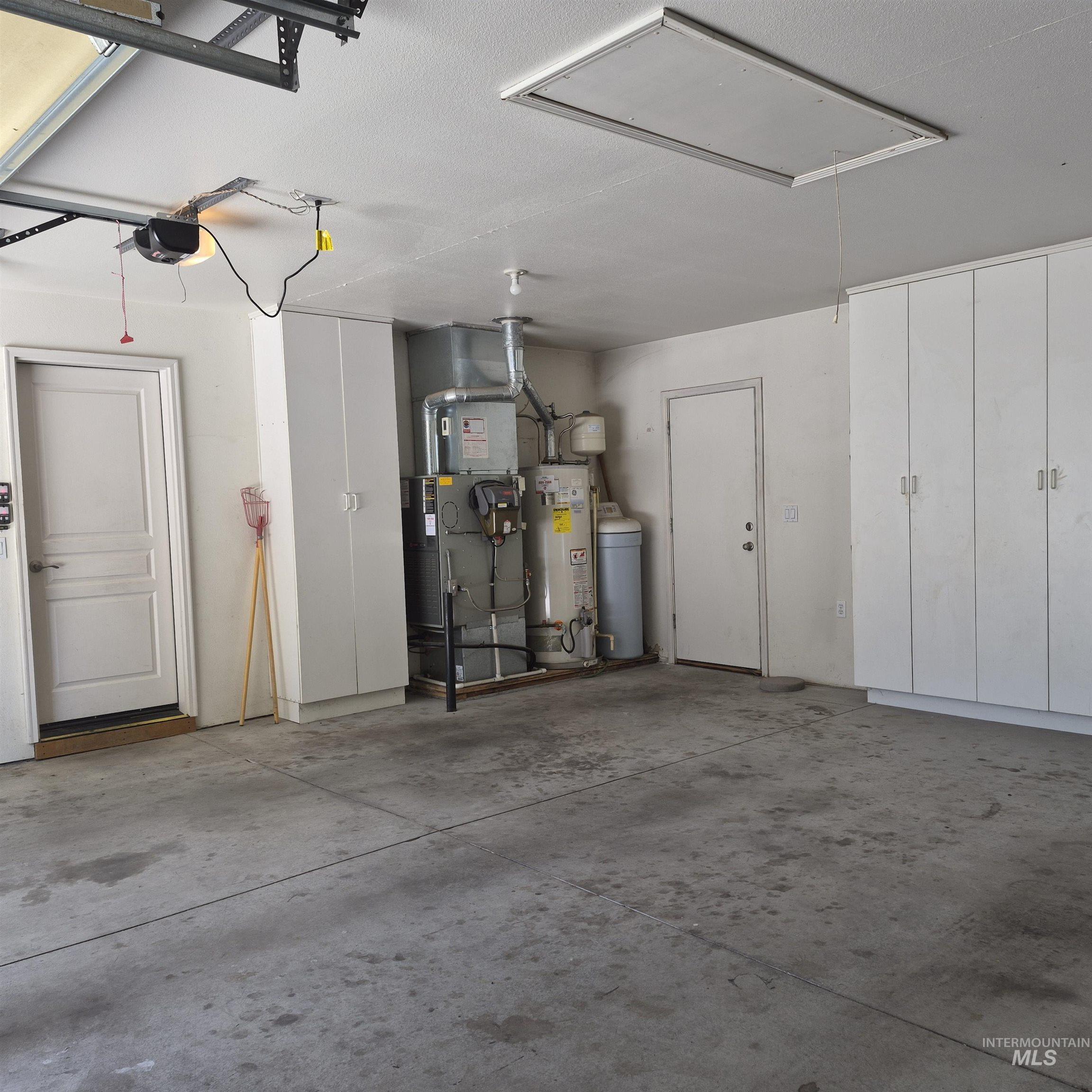 Spacious garage featuring concrete flooring, built-in white cabinetry, an overhead access panel, and a garage door opener system