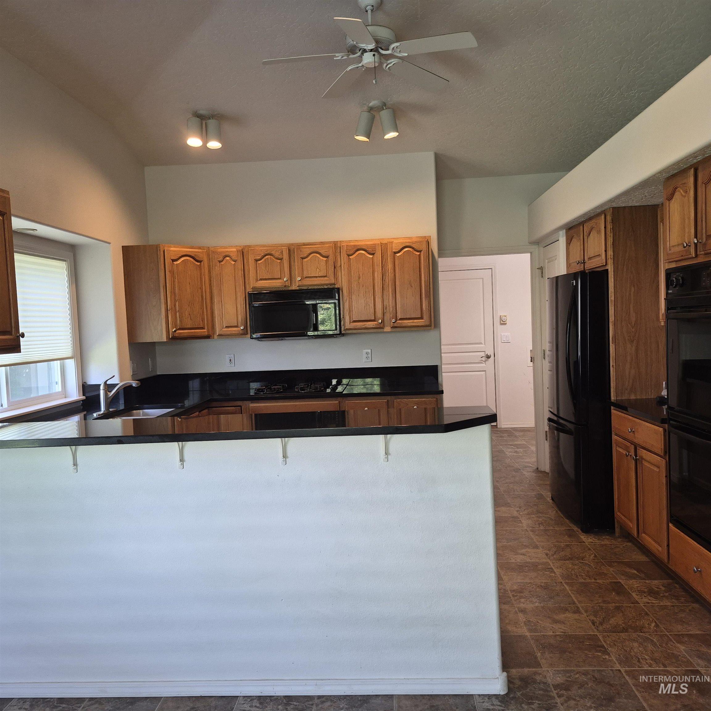 Kitchen featuring wood cabinetry, black countertops, a microwave, an electric range, and a refrigerator