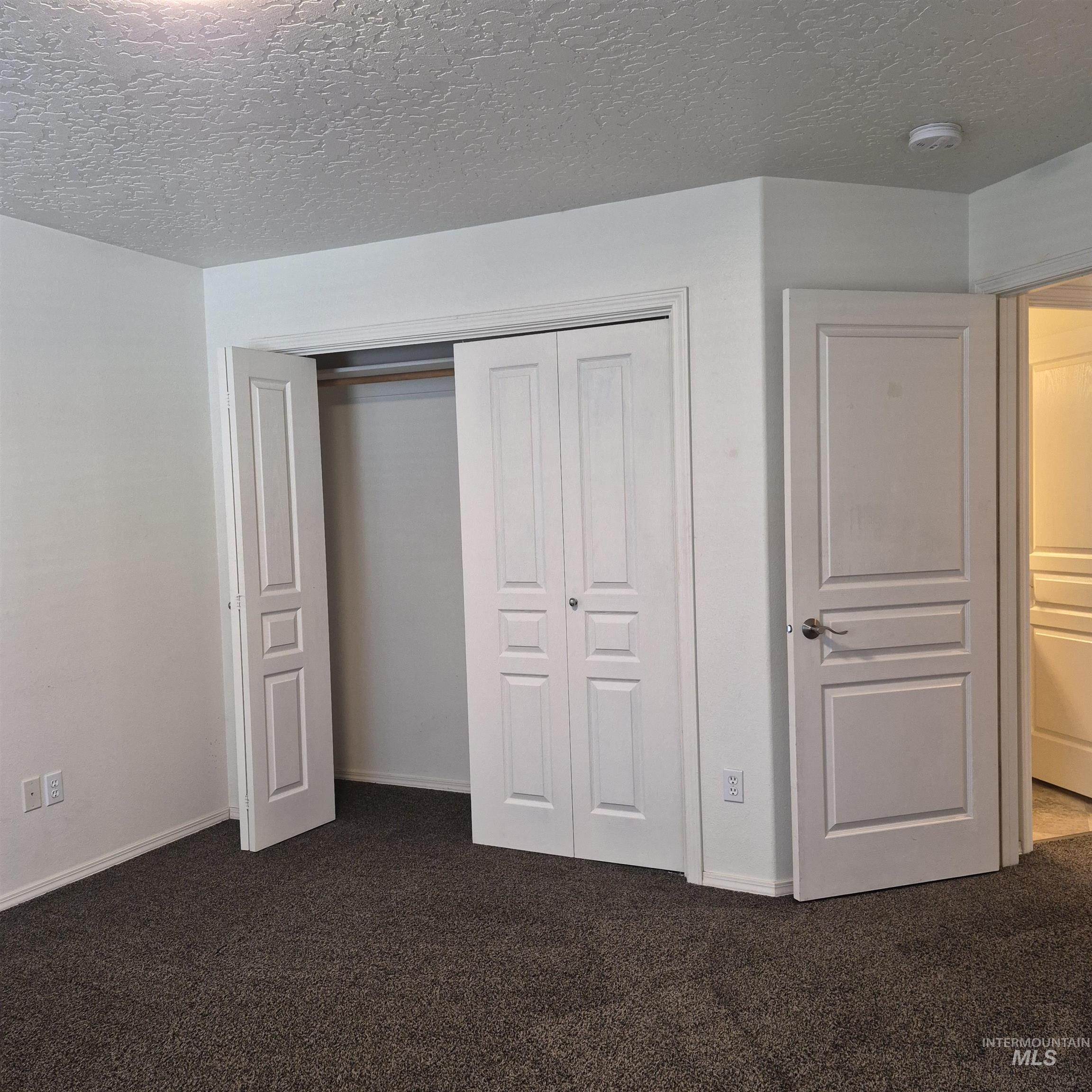 Room featuring light-toned walls, textured ceiling, and dark carpet