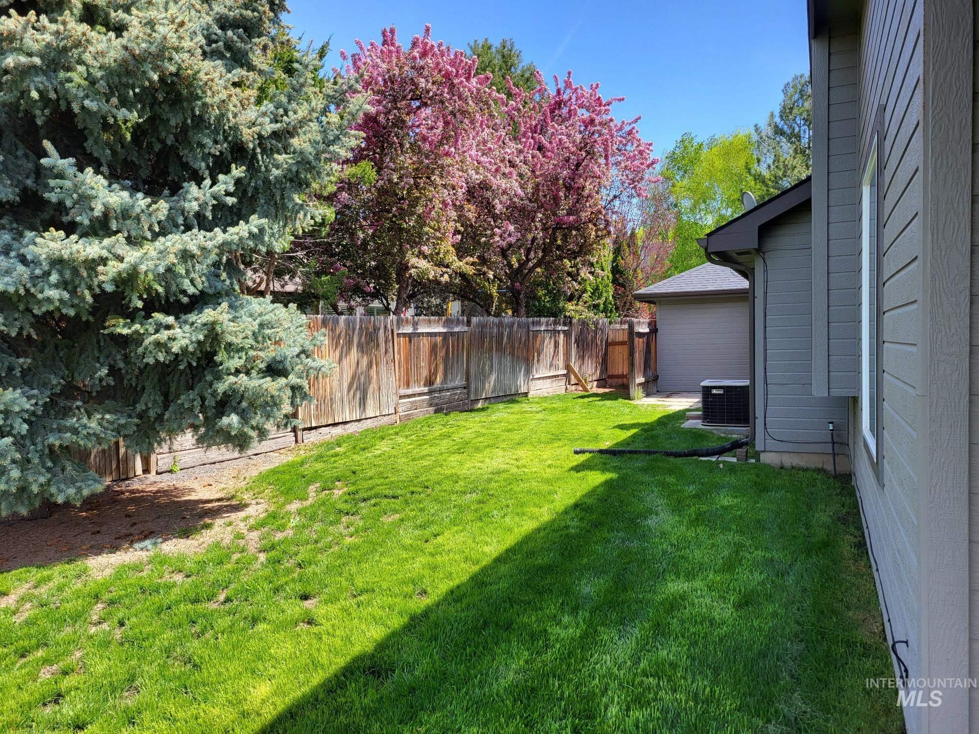 Spacious side yard featuring a lush green lawn, full privacy fencing, and concrete pad.