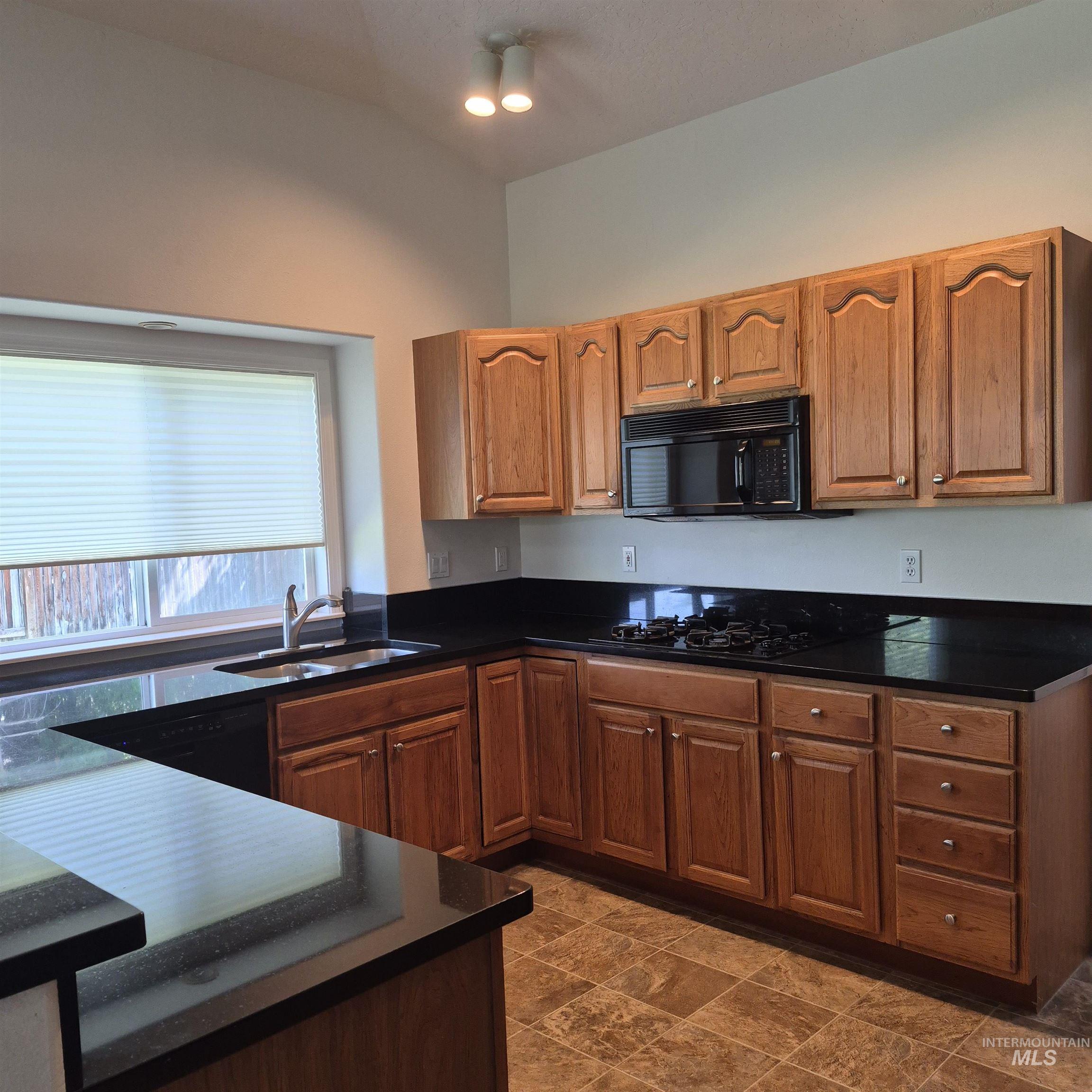 Kitchen featuring wood cabinetry, dark countertops, a built-in microwave, an integrated gas cooktop