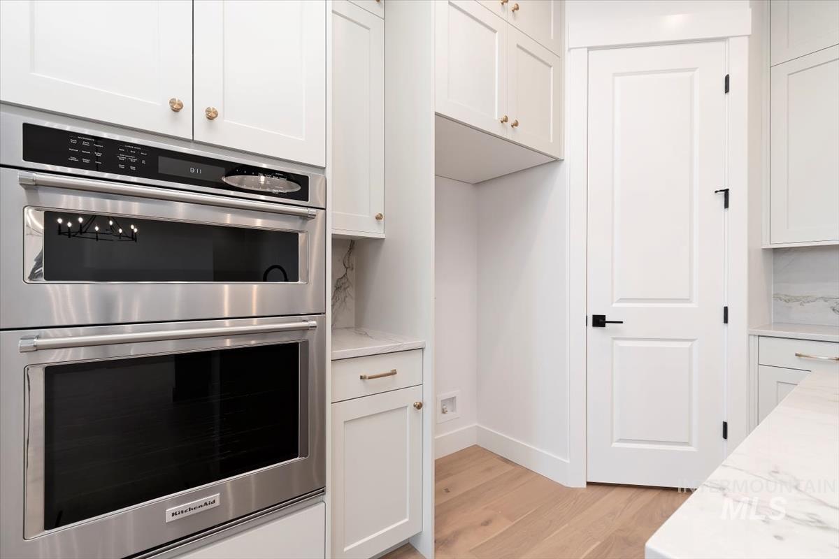 Kitchen with double oven, white cabinetry, light wood finished floors, and light stone countertops