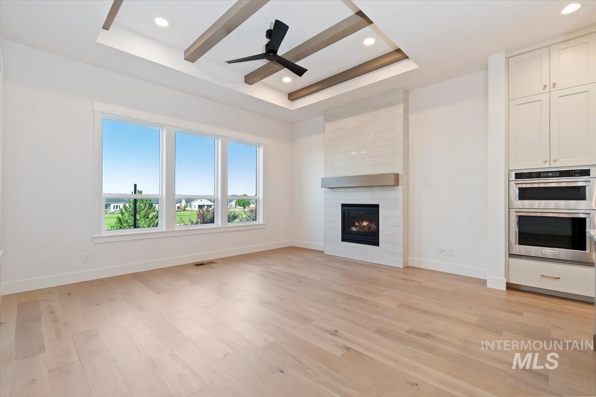 Unfurnished living room featuring a tray ceiling, light wood finished floors, a fireplace, recessed lighting, and a ceiling fan