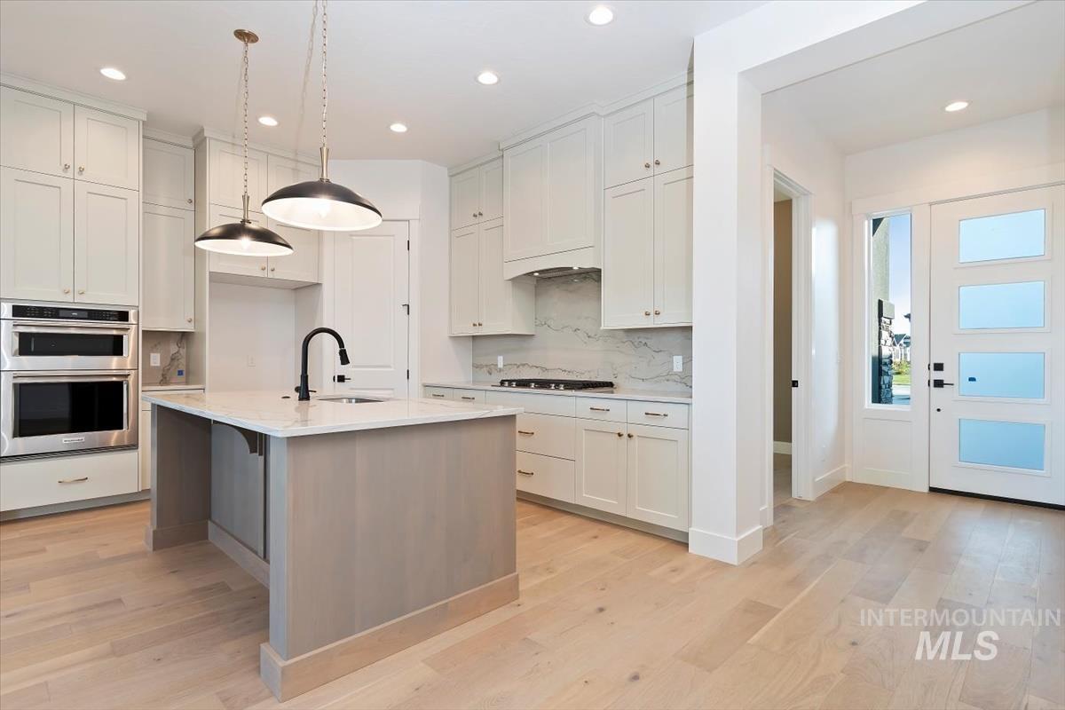Kitchen with white cabinetry, stainless steel appliances, a center island with sink, light wood-style flooring, and hanging light fixtures