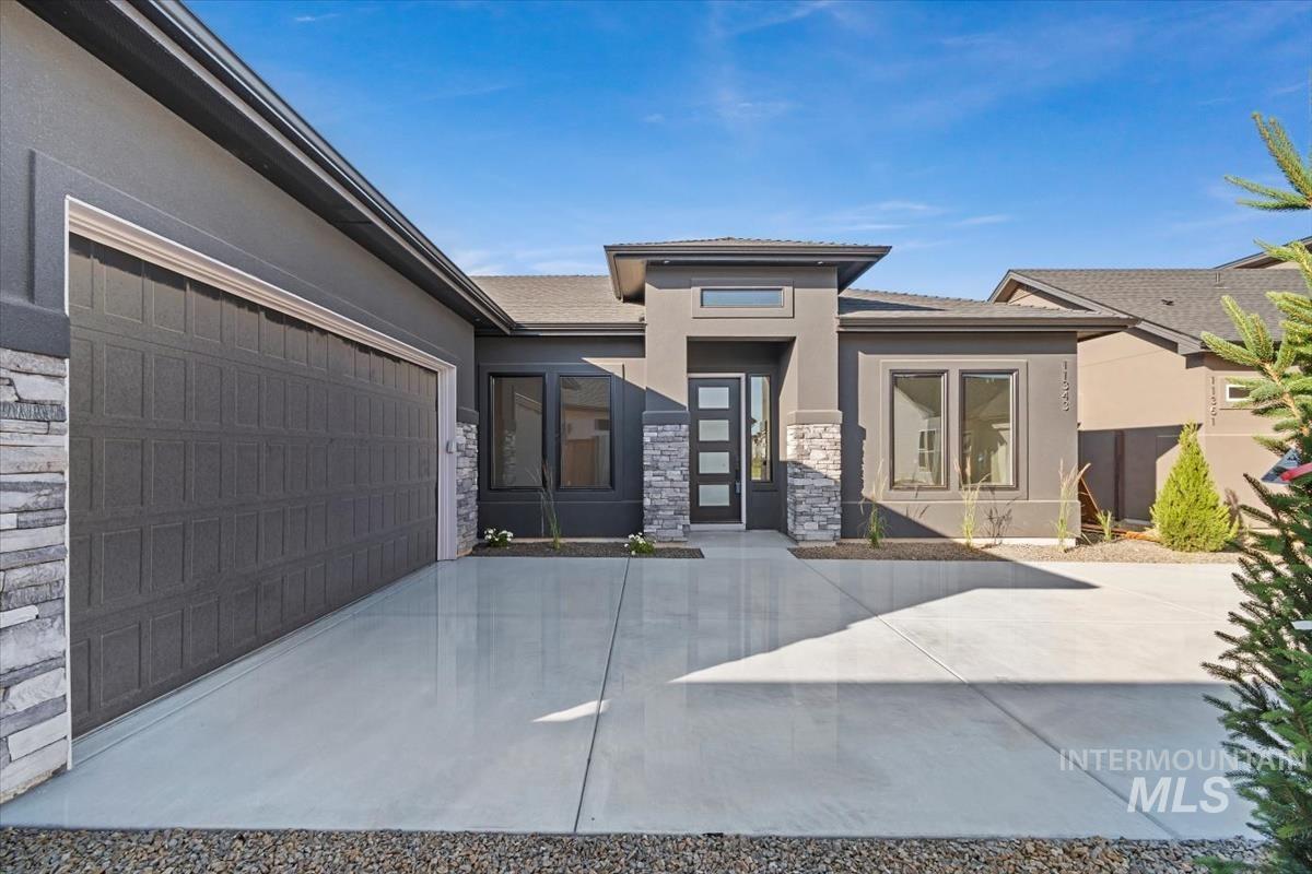 Prairie-style home featuring stone siding, stucco siding, driveway, and an attached garage
