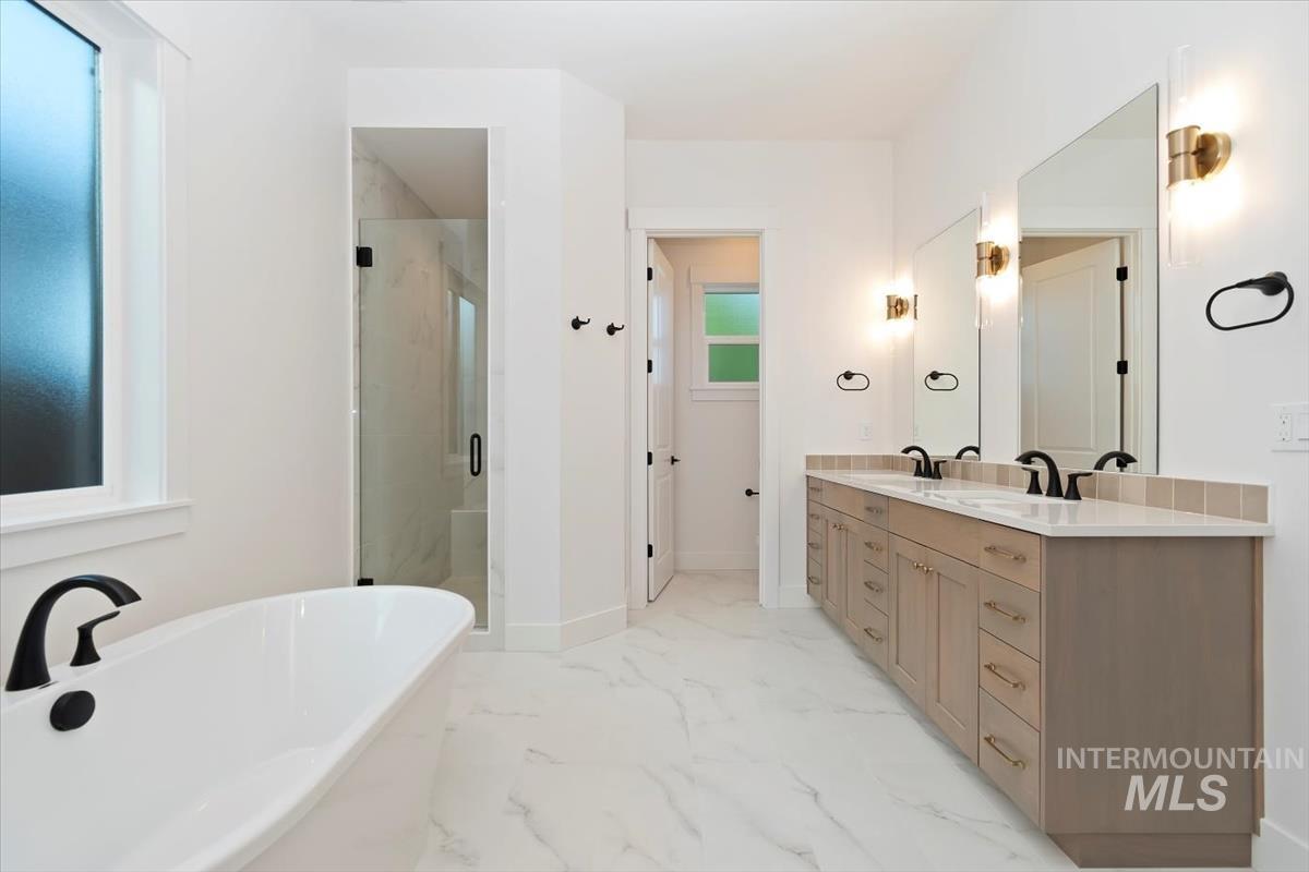 Bathroom with a freestanding tub, double vanity, a marble finish shower, and plenty of natural light
