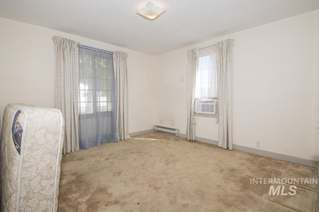 Empty room featuring light colored carpet, cooling unit, and a baseboard radiator