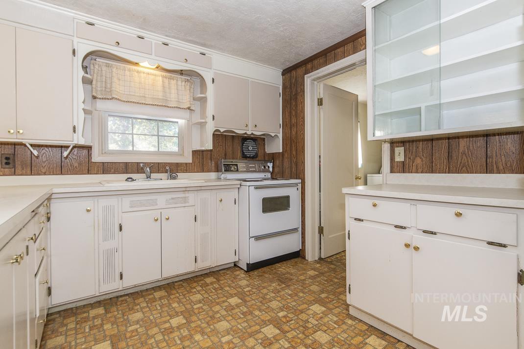 Kitchen with open shelves, white electric range oven, light countertops, white cabinets, and wood walls