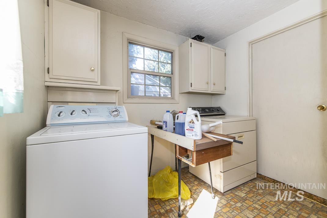 Laundry room featuring cabinet space, washing machine and clothes dryer, a textured ceiling, and brick patterned floors
