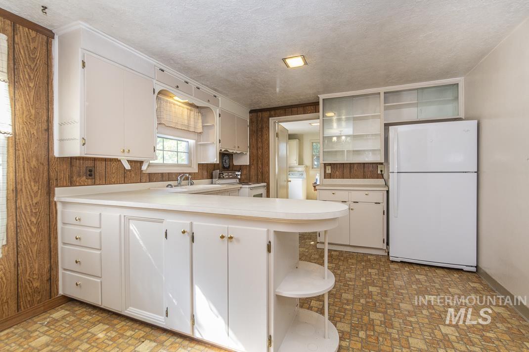 Kitchen with open shelves, a peninsula, white appliances, light countertops, and a textured ceiling