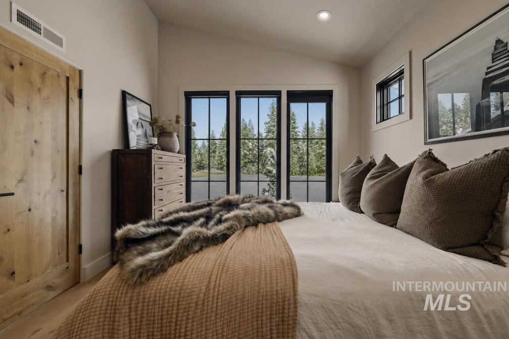 Vaulted ceiling bedroom featuring wood-finish flooring, a natural wood door, and black-framed windows overlooking exterior greenery