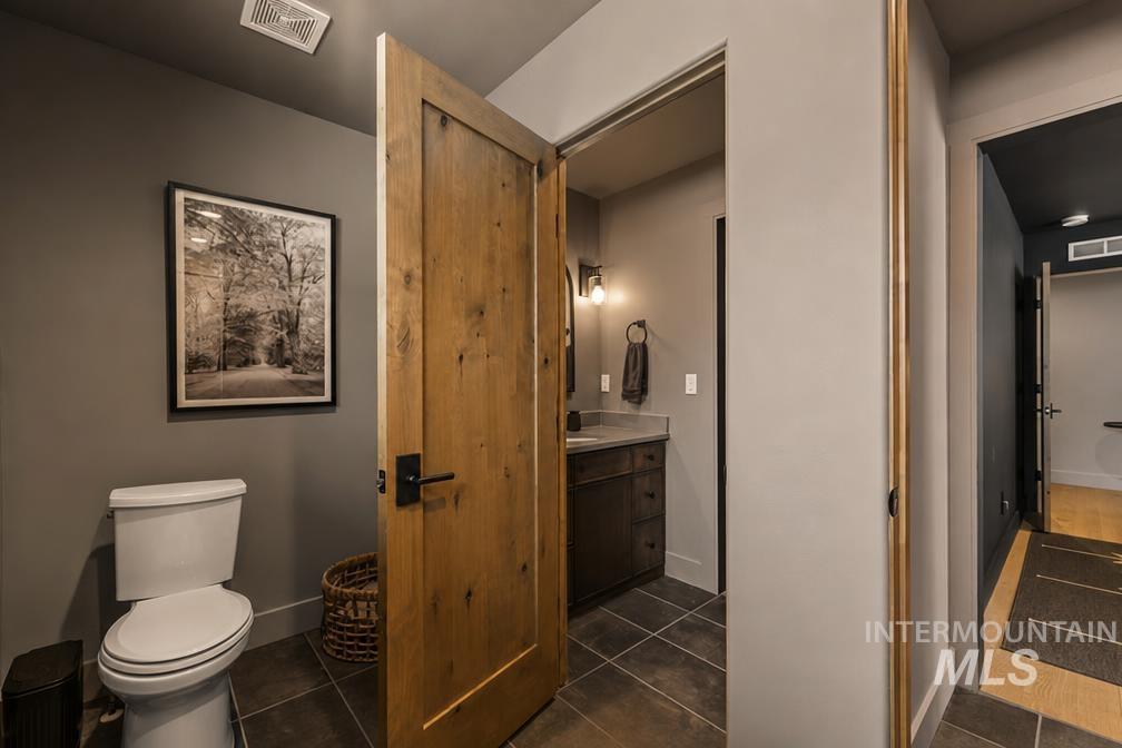 Powder room featuring a natural wood-finish door with black hardware, dark gray tiled flooring, and a modern vanity with a countertop and vessel sink