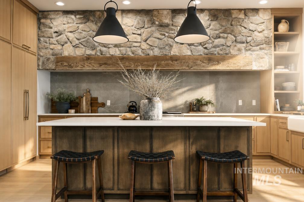 Kitchen featuring a stone accent wall, rustic wood beam, central island with seating, light wood cabinetry, and a white farmhouse sink