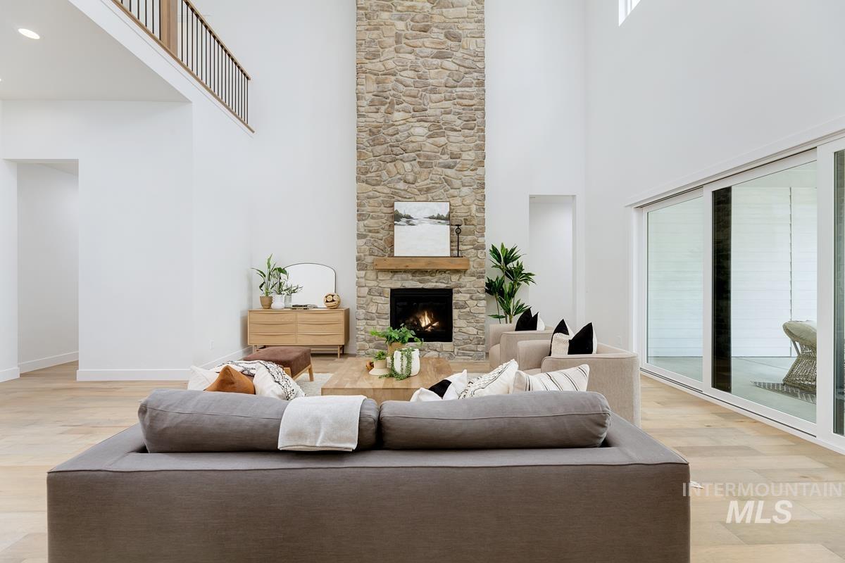 Living room with a high ceiling, light wood-style flooring, and a stone fireplace