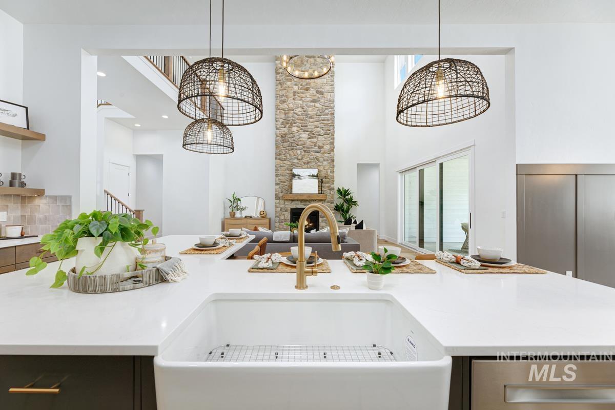 Kitchen with a kitchen island with sink, light stone counters, hanging light fixtures, a high ceiling, and backsplash
