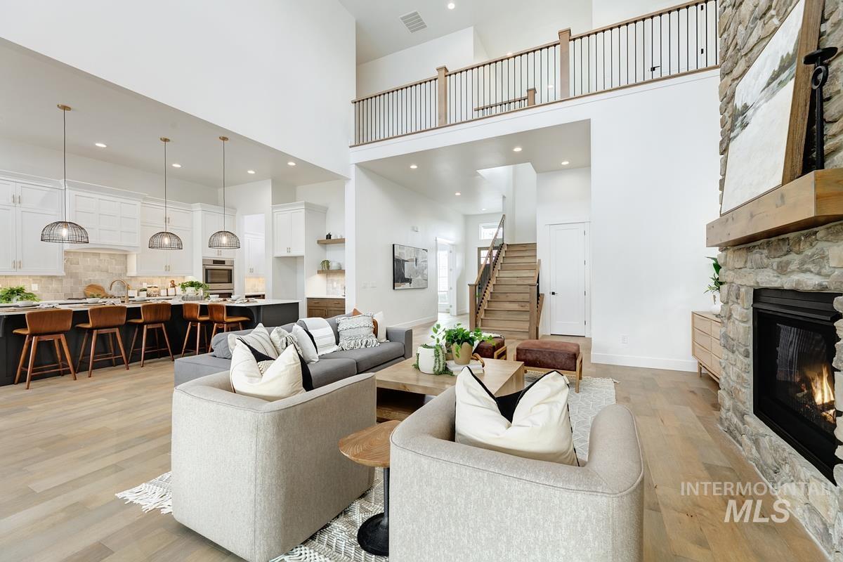 Living room with light wood finished floors, a towering ceiling, a fireplace, stairway, and recessed lighting