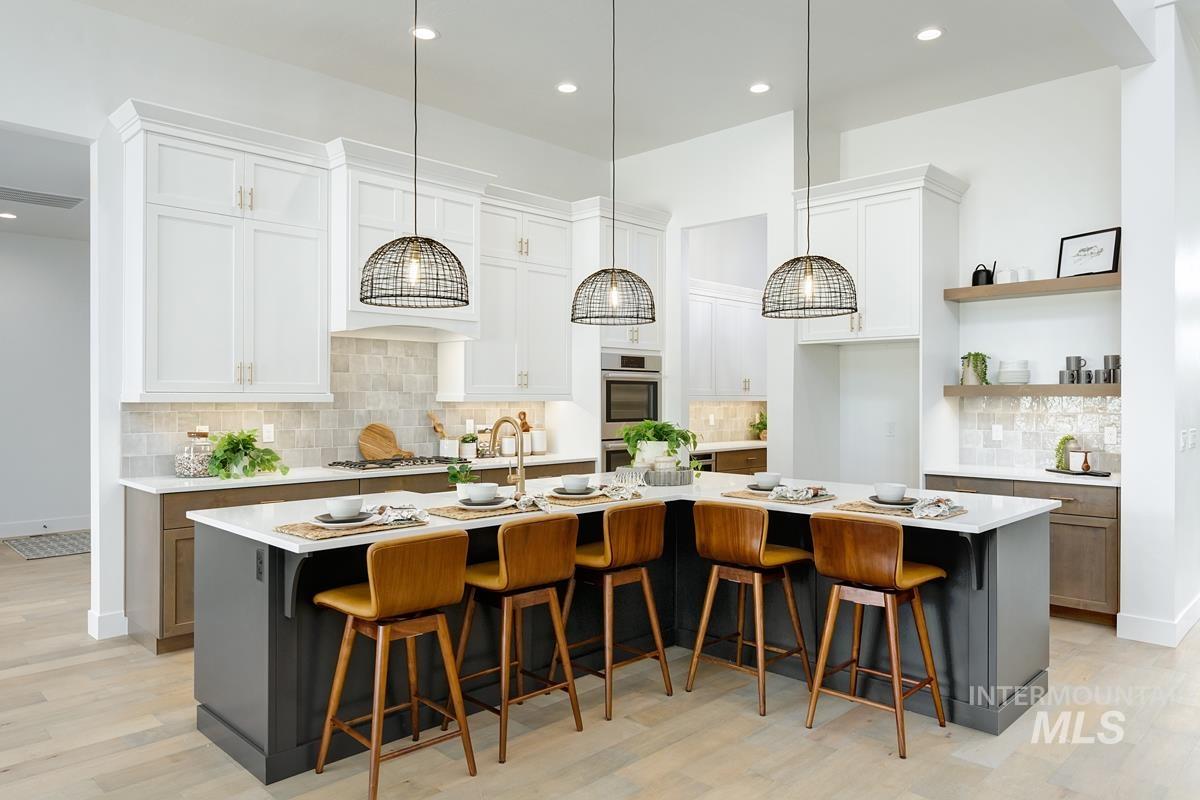 Kitchen with a kitchen breakfast bar, tasteful backsplash, a large island with sink, white cabinets, and recessed lighting