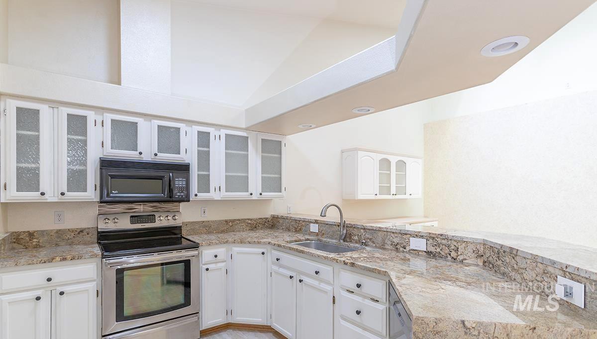 Kitchen with electric range, white cabinetry, black microwave, light stone counters, and a peninsula