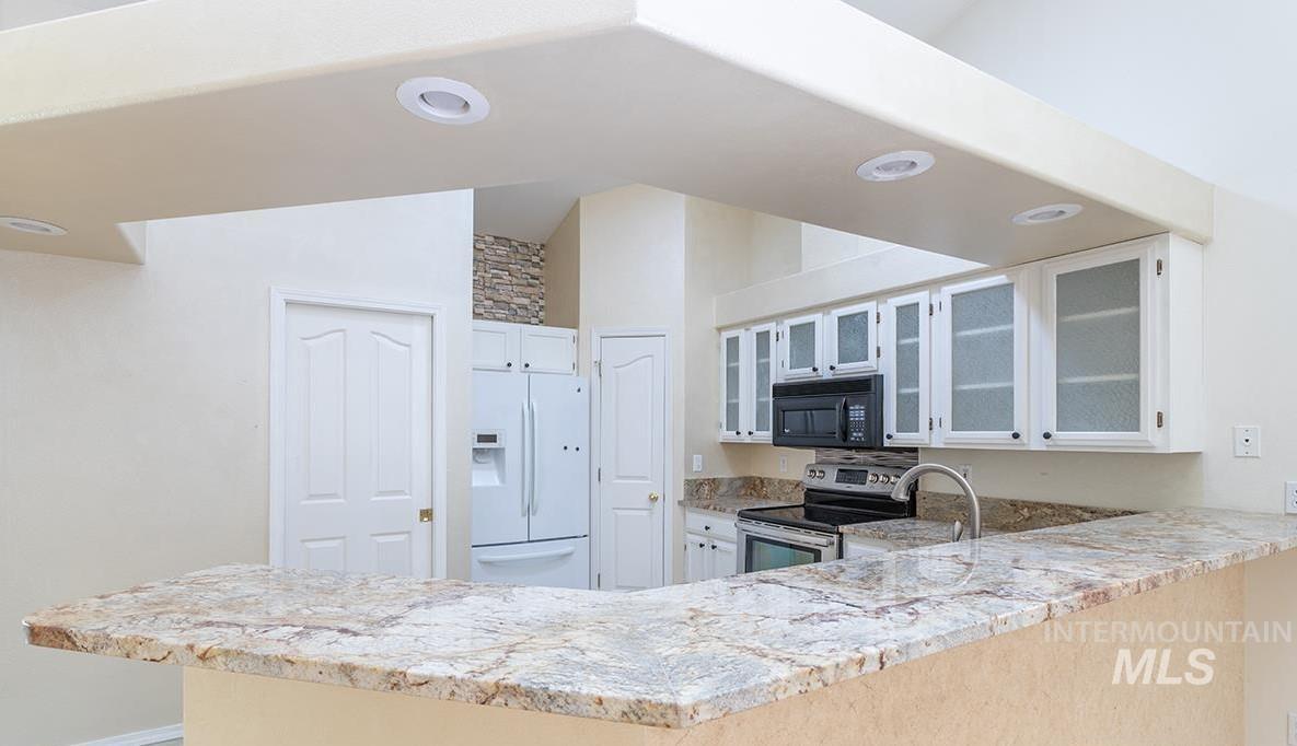 Kitchen with a peninsula, glass insert cabinets, light stone countertops, white refrigerator with ice dispenser, and electric stove