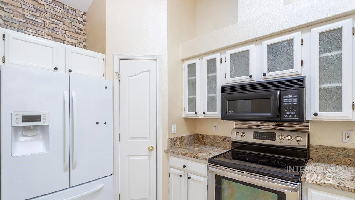 Kitchen featuring white fridge with ice dispenser, stainless steel electric stove, white cabinets, light stone countertops, and black microwave