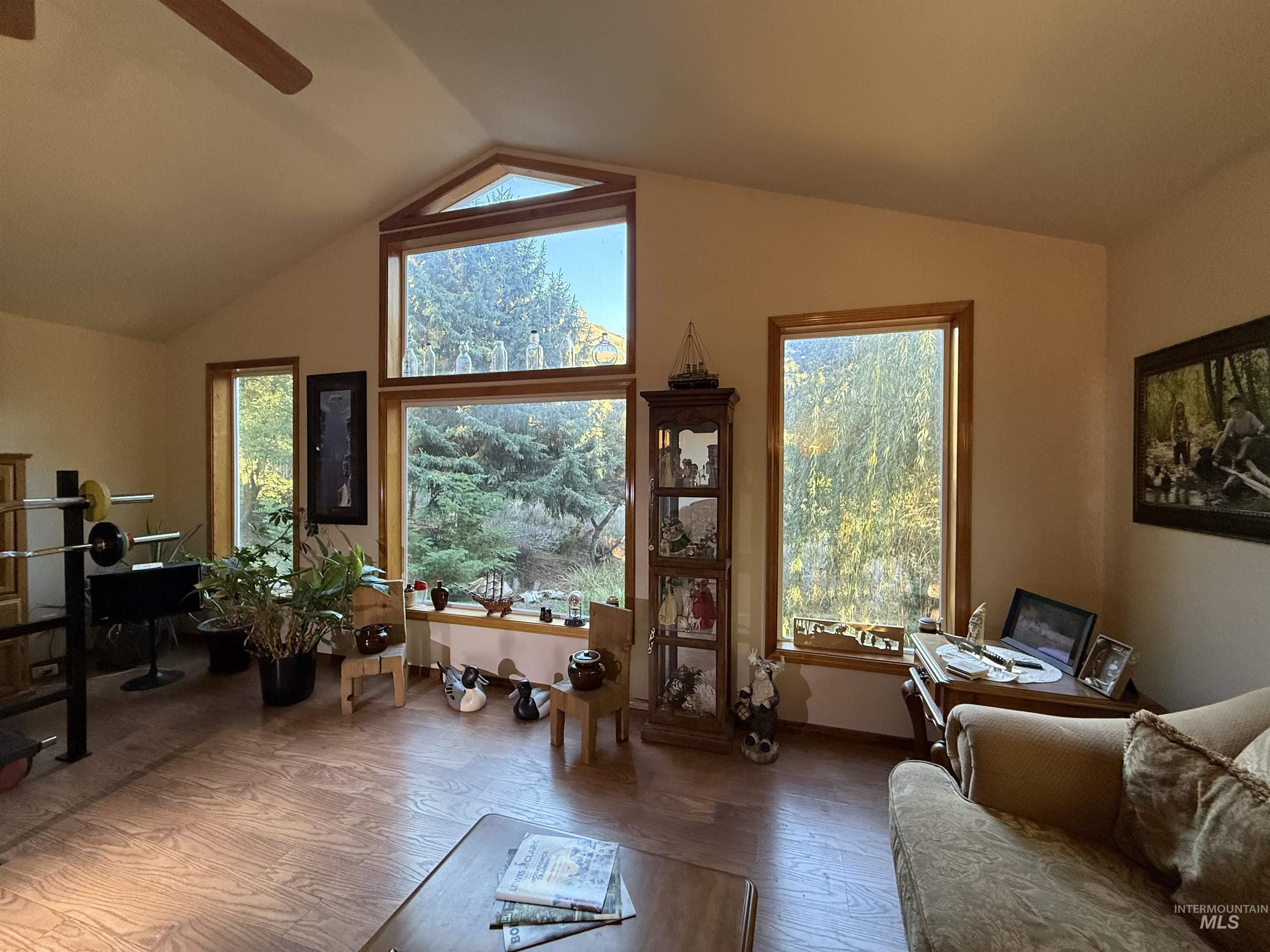 Living area with wood finished floors, healthy amount of natural light, vaulted ceiling, and ceiling fan
