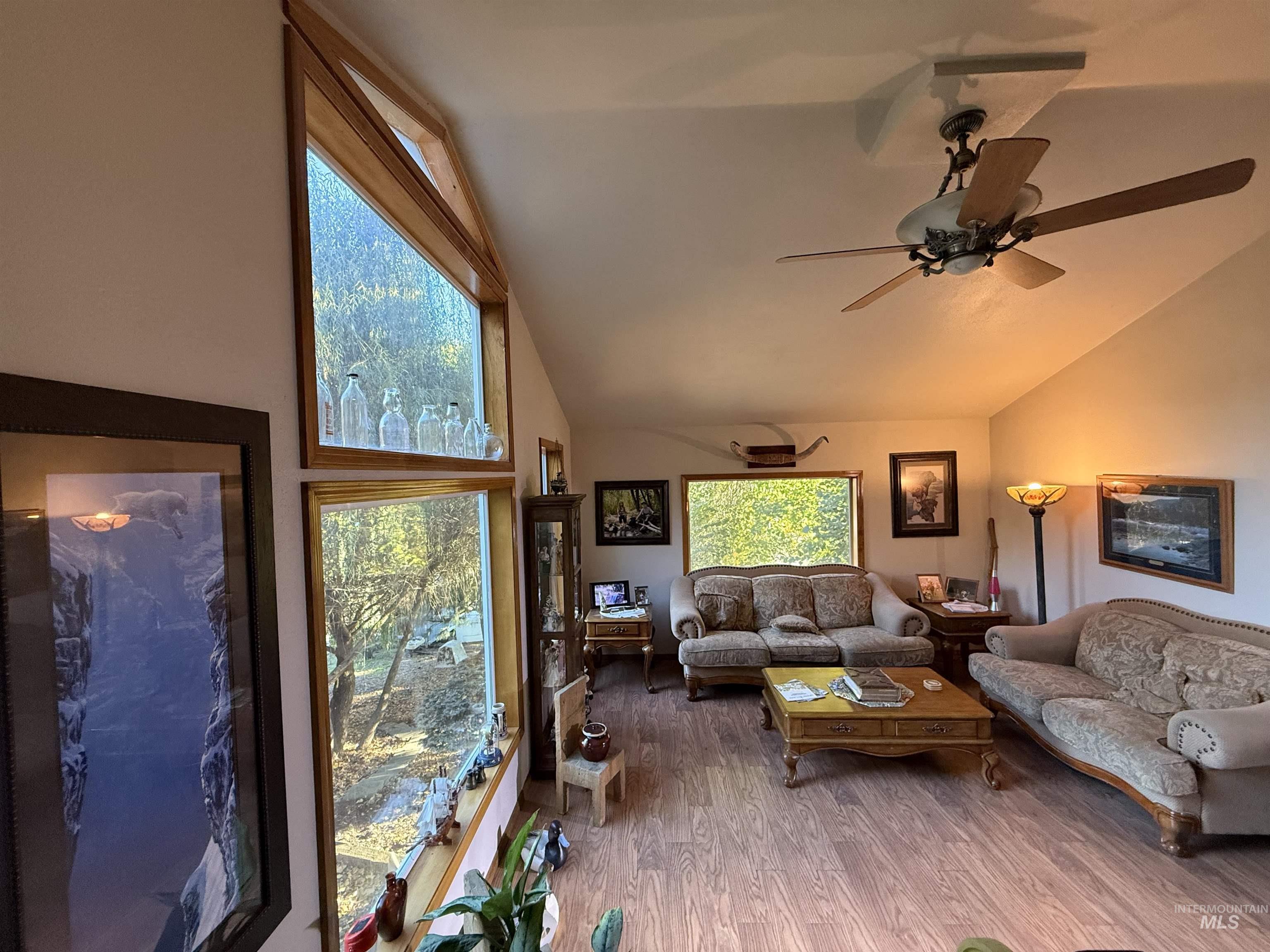 Living room with wood finished floors, high vaulted ceiling, and a ceiling fan