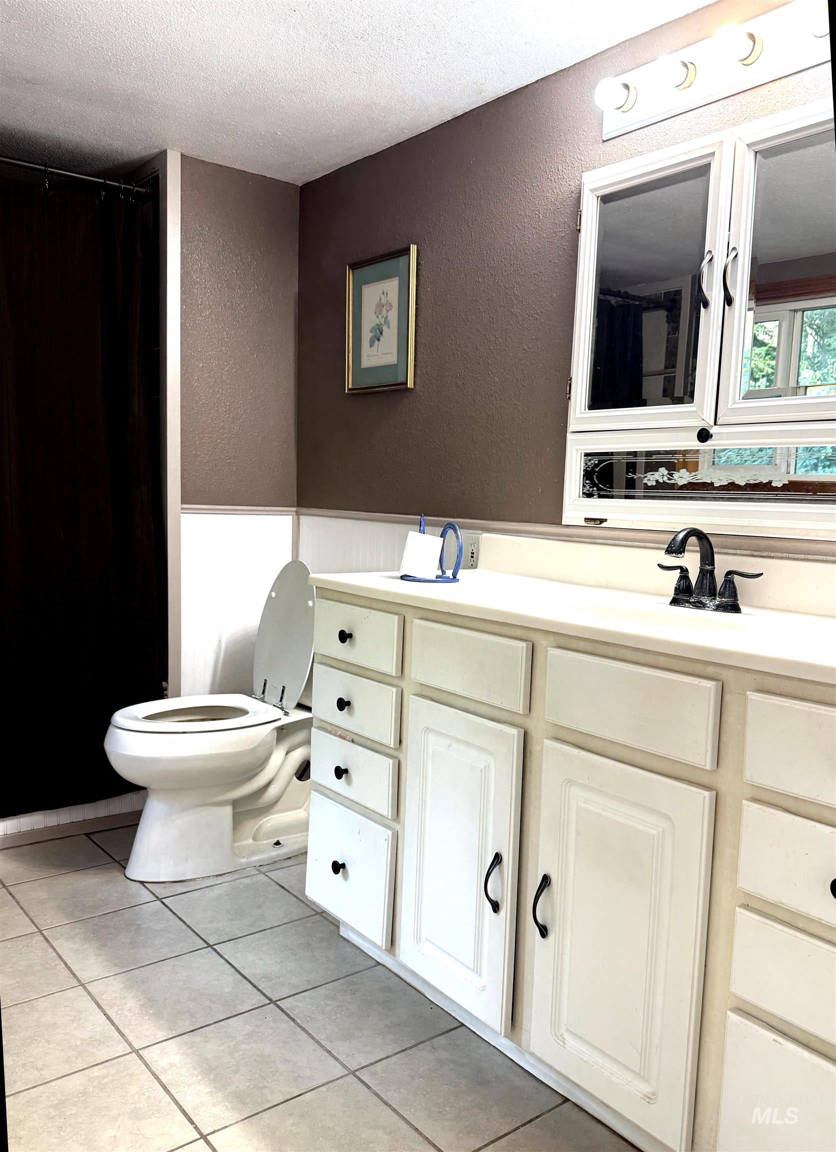 Full bath featuring a textured wall, vanity, light tile patterned floors, a textured ceiling, and curtained shower