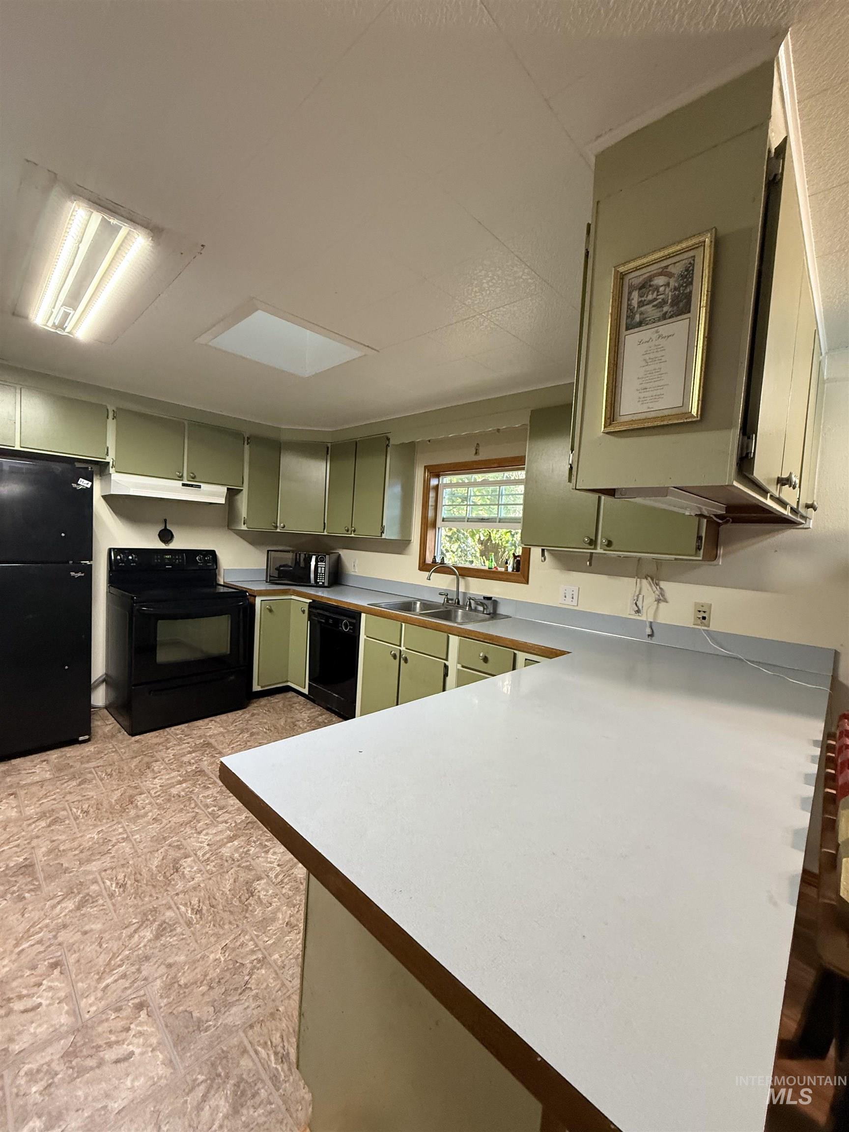 Kitchen with green cabinets, black appliances, light countertops, a peninsula, and under cabinet range hood