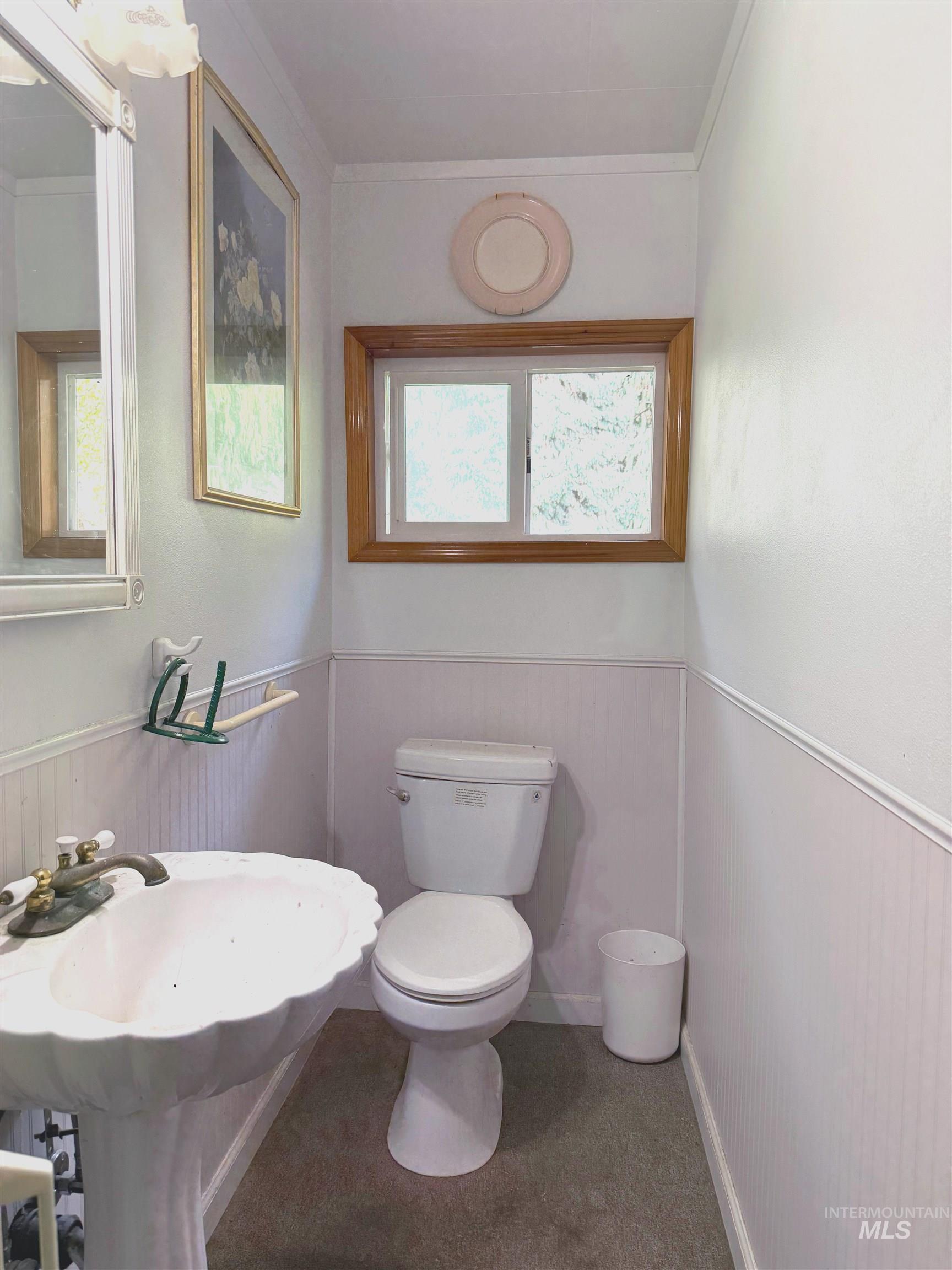 Half bathroom with a wainscoted wall and crown molding