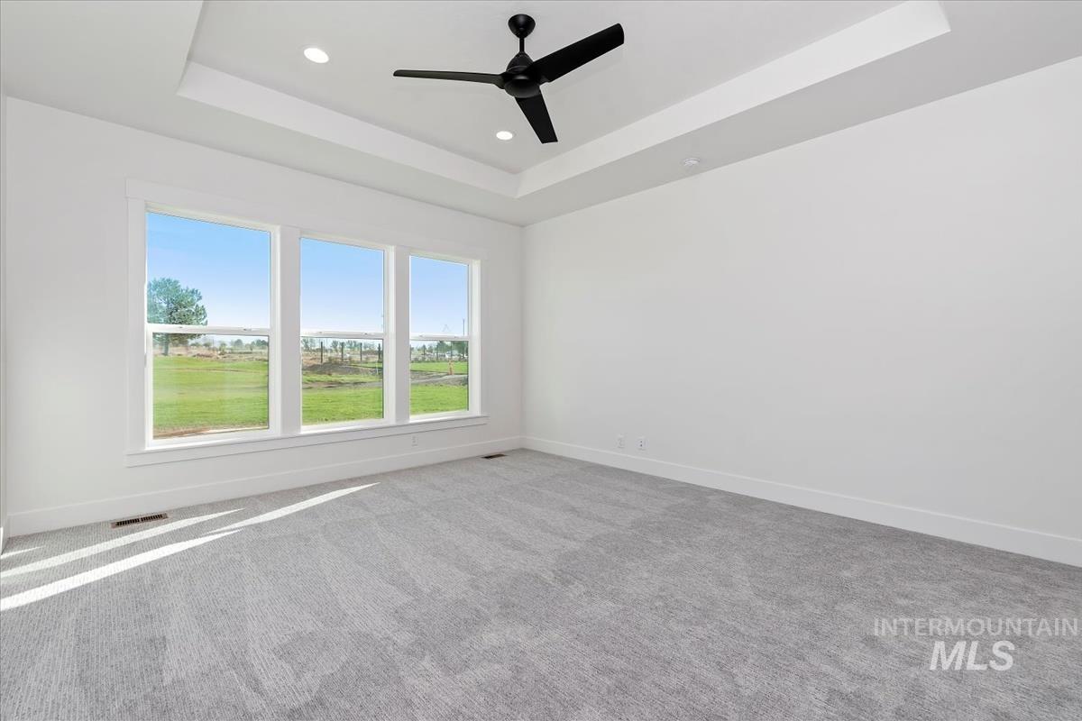Spacious room featuring three large windows, tray ceiling, recessed lighting, and a contemporary ceiling fan