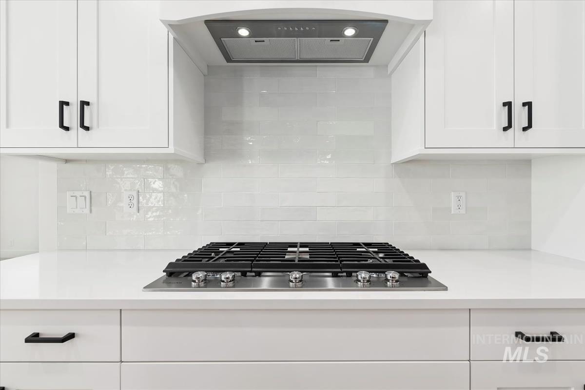 Modern kitchen featuring white shaker cabinetry with matte black hardware, a built-in stainless steel gas cooktop, sleek range hood, and a light-toned subway tile backsplash
