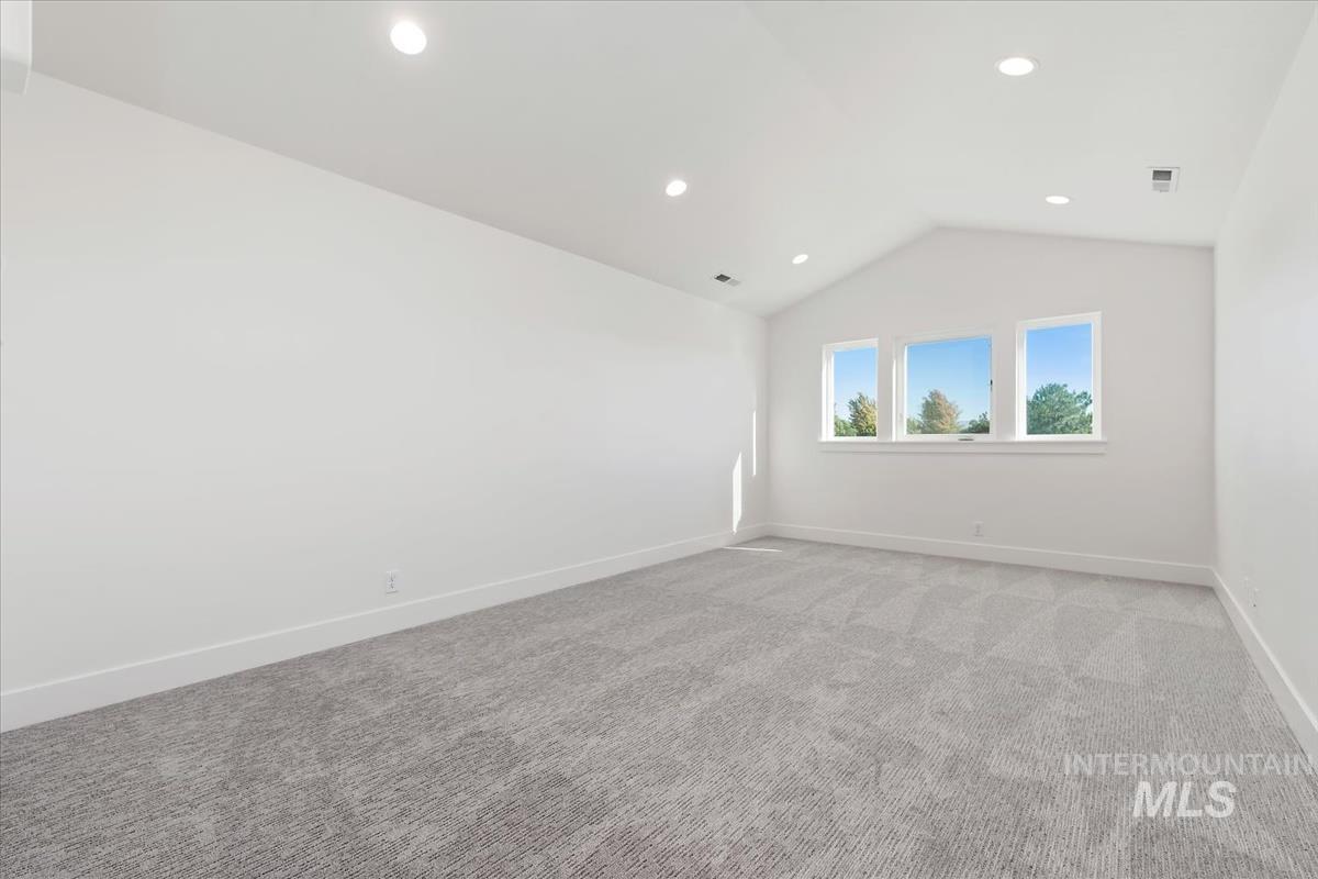 Vaulted ceiling room featuring three rectangular windows, recessed lighting, and a neutral patterned carpet