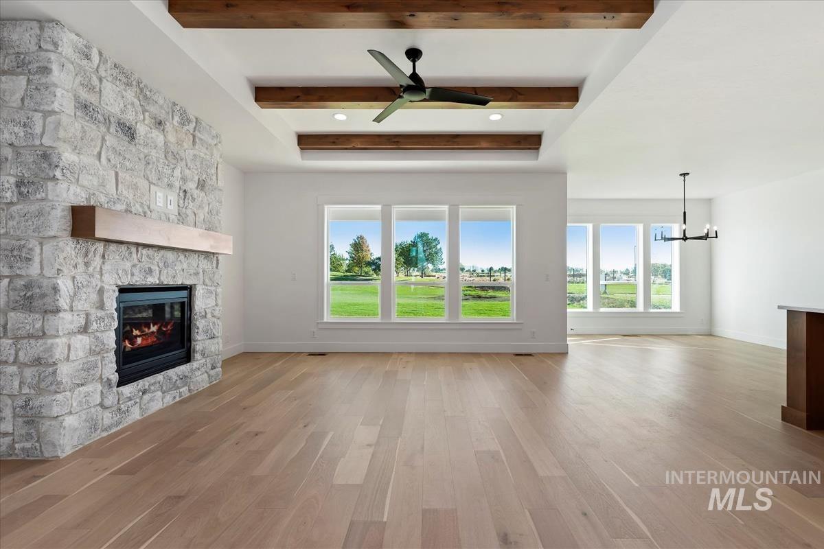 Living area featuring a stone-faced fireplace with a wood mantel, wood-finish flooring, a tray ceiling with exposed wood beams, and a ceiling fan