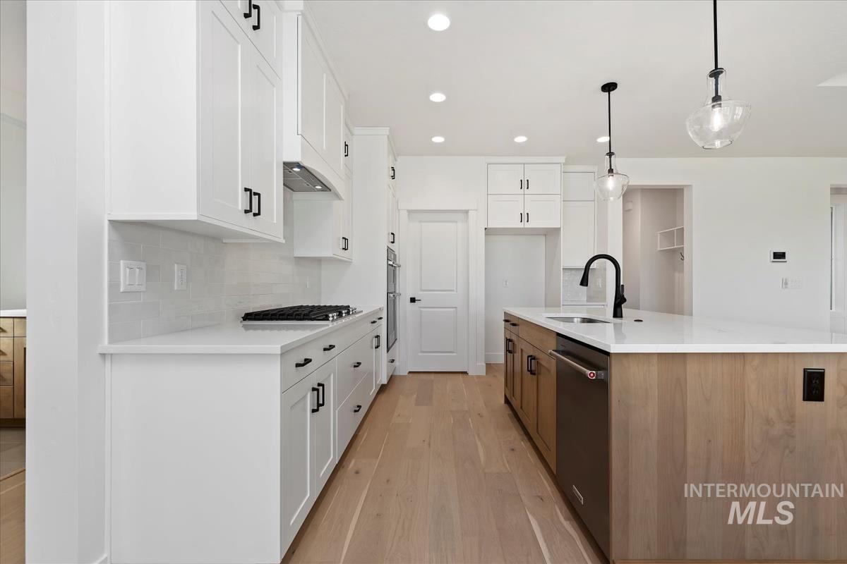 Modern kitchen featuring white shaker cabinetry, light wood-finish flooring, a center island with a built-in sink, and stainless steel appliances