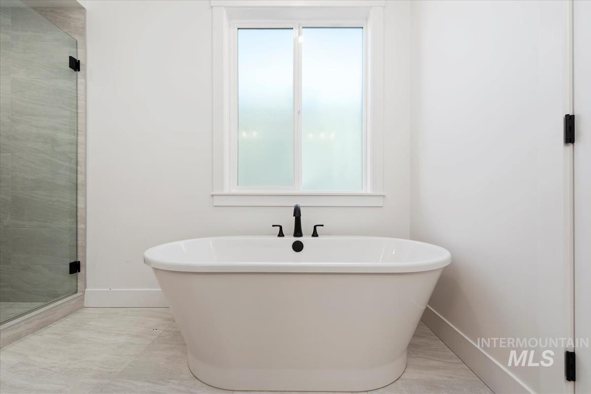 Freestanding soaking tub with a floor-mounted matte black faucet, set against white walls and light-toned tile flooring