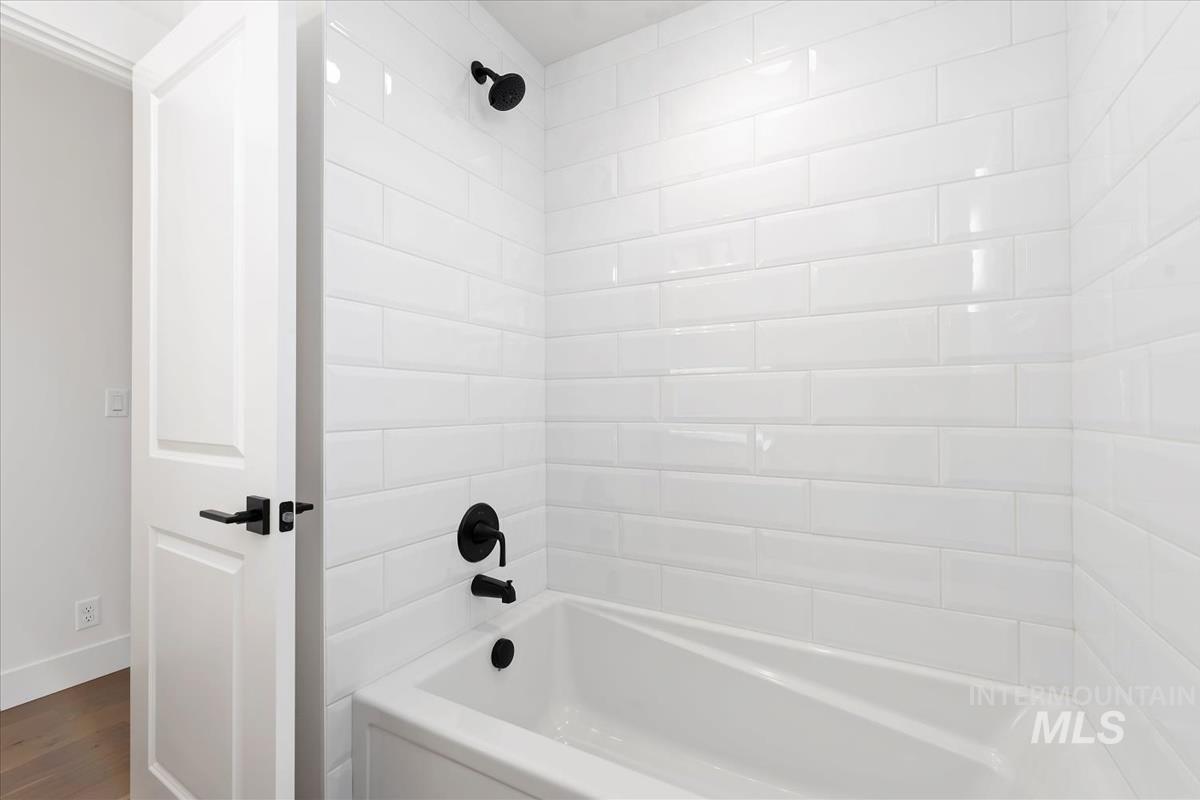 Bathtub and shower combination featuring glossy white subway tile surround and matte black fixtures