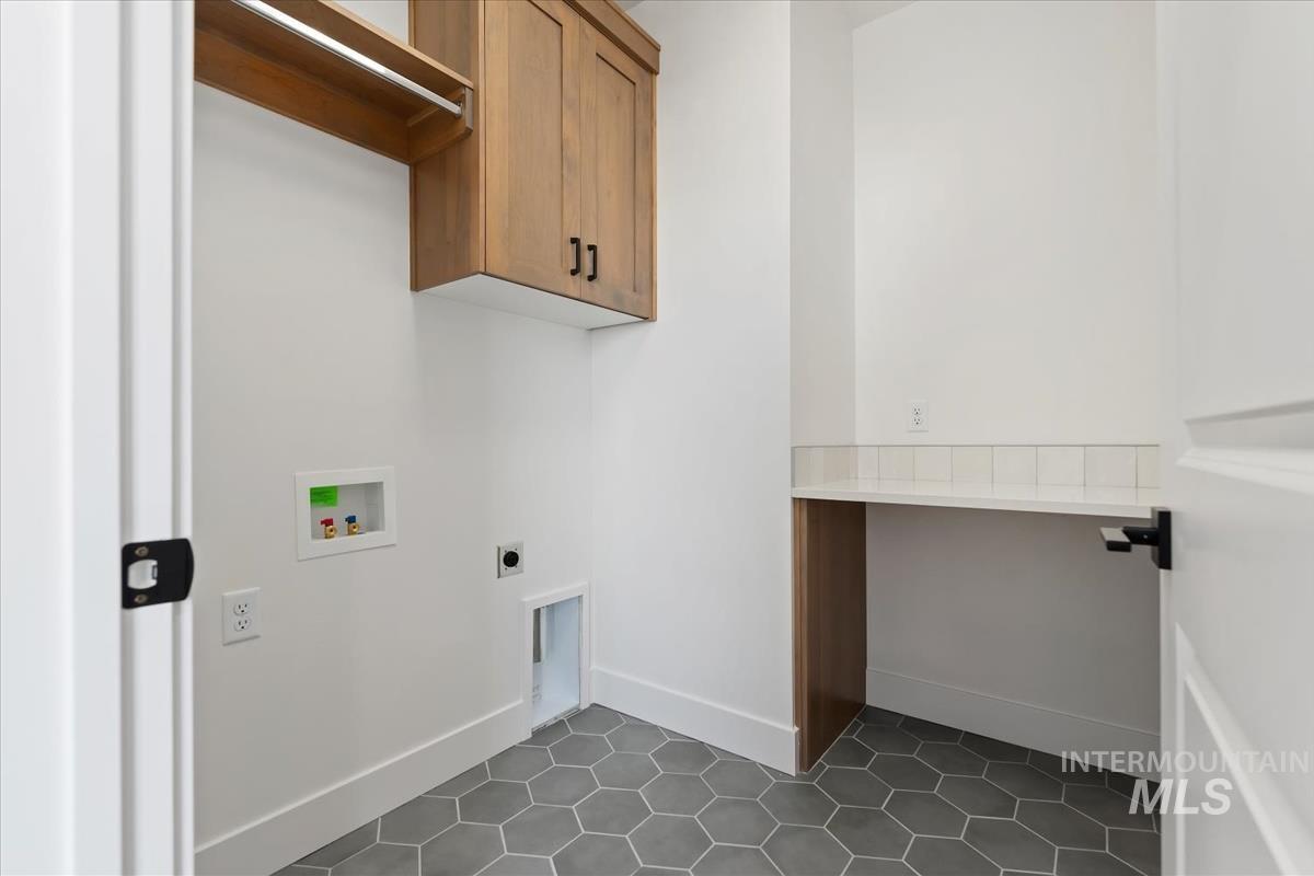 Laundry area featuring hexagonal floor tiling, built-in wooden cabinetry, an integrated clothes rod, a white countertop with a subway tile backsplash, and a dedicated appliance hookup