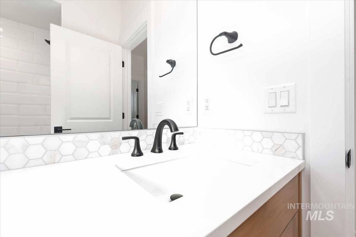 Vanity featuring a white countertop with integrated sink, matte black faucet, and a hexagonal tile backsplash