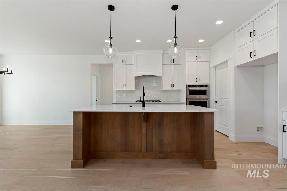 Modern kitchen featuring a large wood-finish island with a white countertop, two pendant lights, and light wood-finish flooring