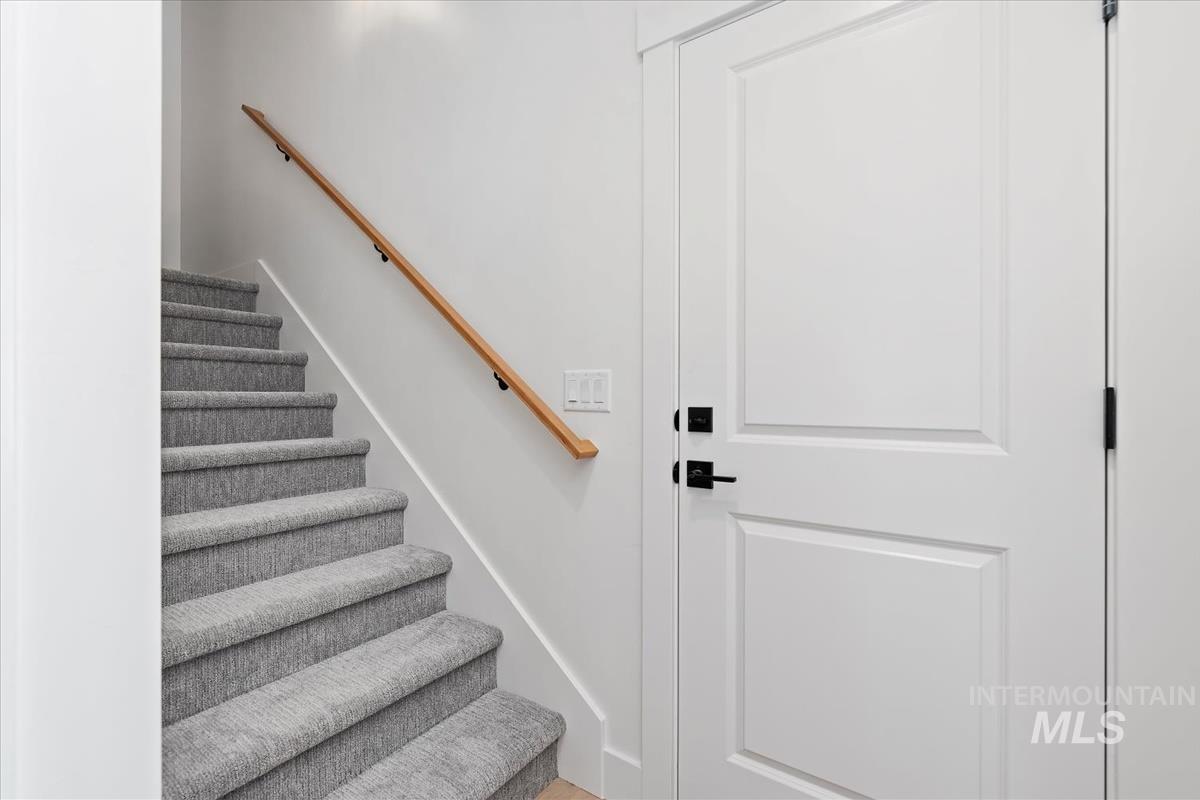 Carpeted staircase with a wood handrail, featuring white walls and a paneled door with matte black hardware