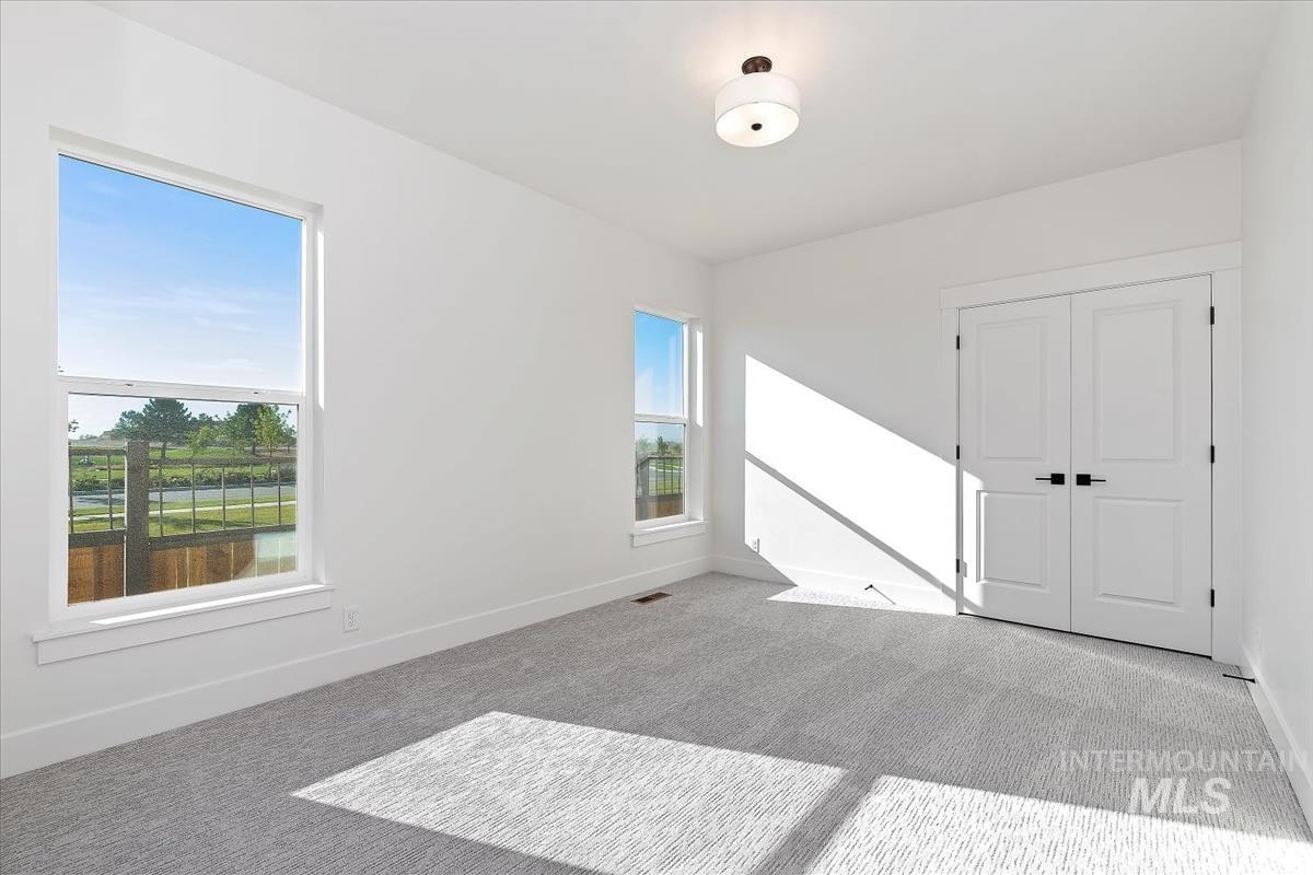 Bright room featuring two large windows, white walls, gray textured carpet, a flush-mount ceiling light fixture, and double doors with matte black hardware