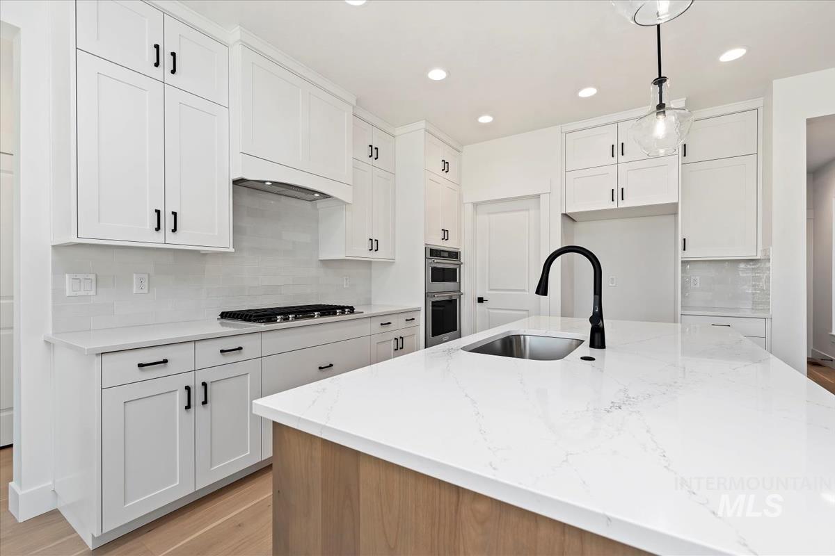 Kitchen featuring an expansive island with a matte black faucet and undermount sink, white shaker cabinetry with black hardware, a gas cooktop, and built-in double ovens