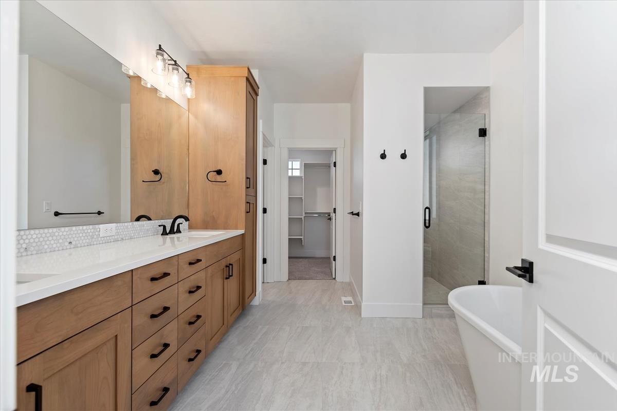 Spacious bathroom featuring a dual vanity with wood cabinetry, white countertops, and hexagonal tile backsplash