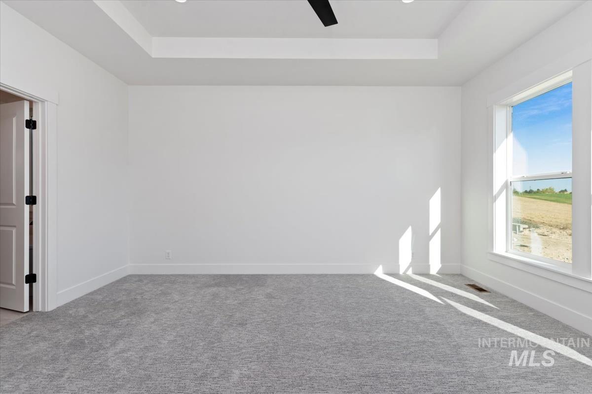 Spacious room featuring light gray carpeting, a tray ceiling, and a black ceiling fan