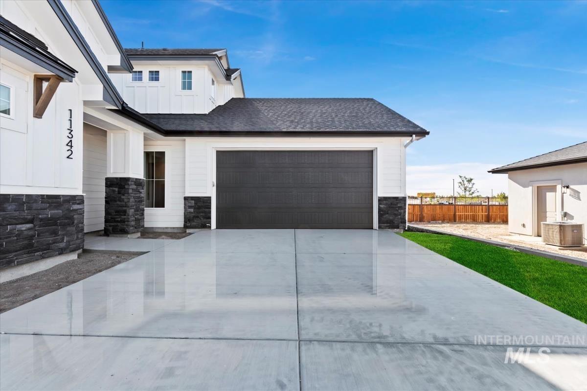 Modern farmhouse exterior with white board-and-batten siding, a dark asphalt shingle roof, and stone veneer accents